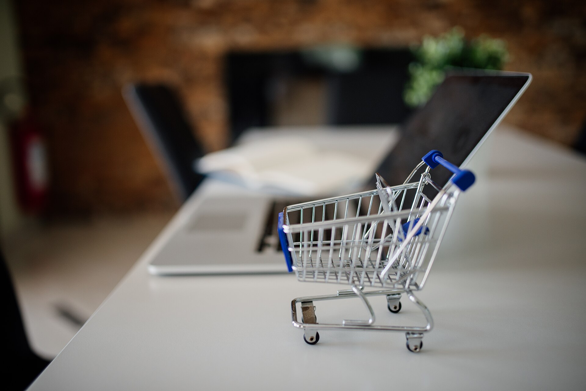 A miniature shopping cart next to a laptop, showing online shopping on a computer